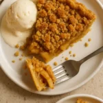 Slice of apple crumble pie with vanilla ice cream showing layered interior
