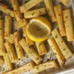 Golden roasted parsnips with herbs on white platter showing perfect caramelization